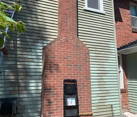 Before: green siding around a red brick chimney with visible surface wear