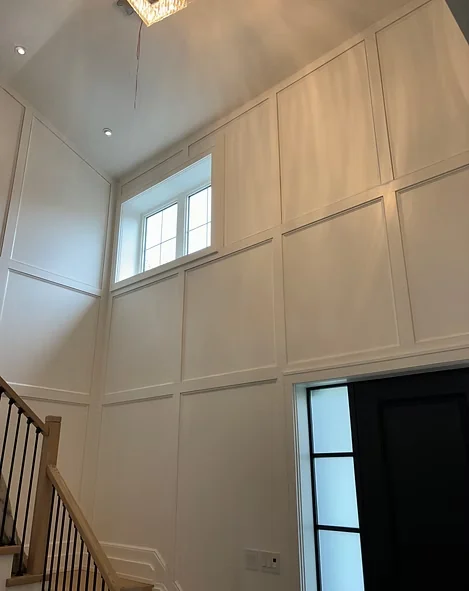 Tall foyer with white panelled walls, staircase and high windows