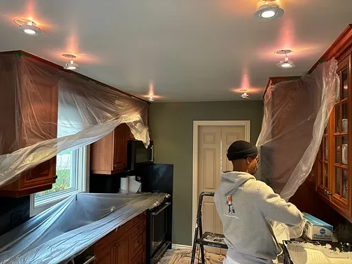 Kitchen preparation with cabinets masked in plastic and a painter at work