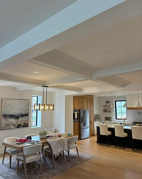 Open living and dining area with pale ceiling beams and protected furniture