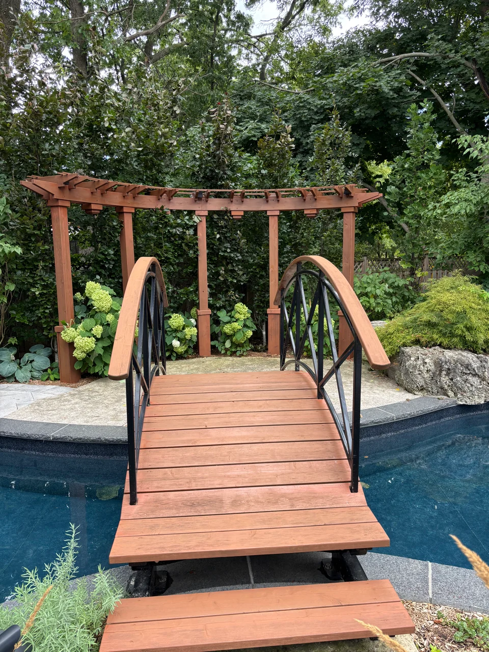 Warm brown stained footbridge with wood railings over a swimming pool