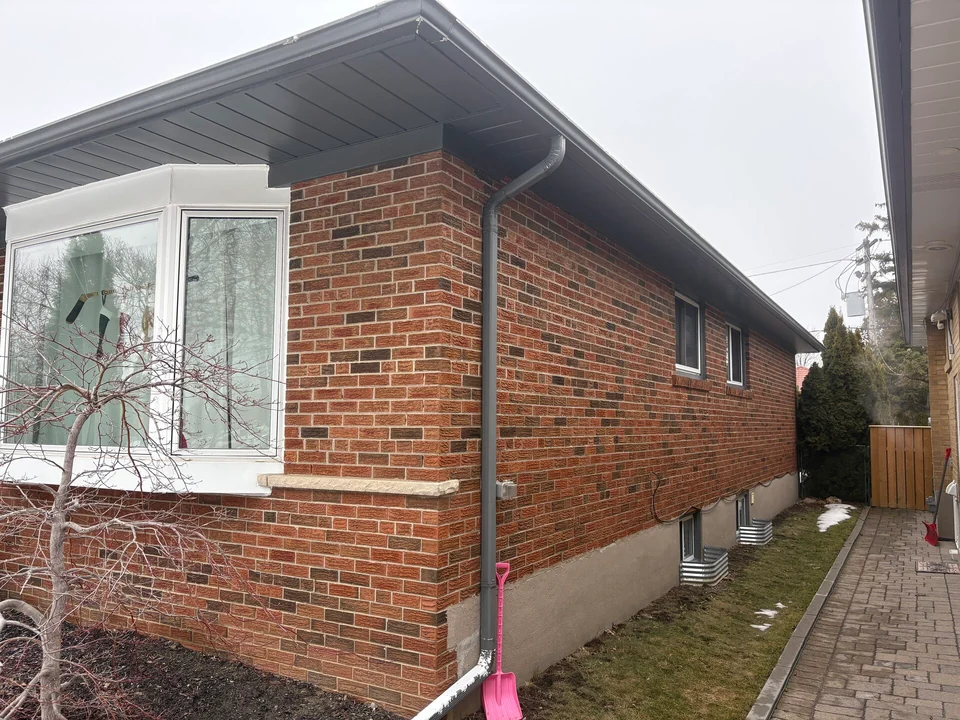 Before: grey soffit along the side wall of a brick bungalow