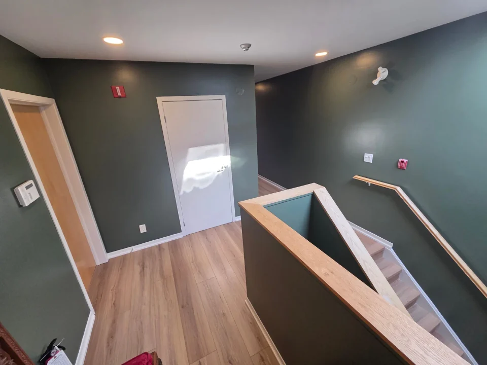 After: deep green stairwell walls with white doors and natural wood handrails